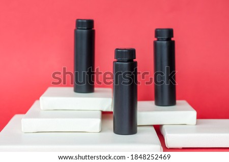 Black bottles of cream stand on white multi-level stands. Black bottles on a red background. Skin care, Moisturizing and nourishing or sunscreen. The industry of cosmetic beauty products