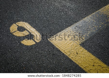 sign on the asphalt, yellow painted number nine on grey street, yellow lines like a corner on the road, space for text 
