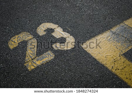 sign on the asphalt, yellow painted number twenty three on grey street, yellow lines like a corner on the road, space for text 
