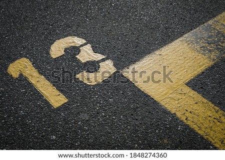 sign on the asphalt, yellow painted number thirteen on grey street, yellow lines like a corner on the road, space for text 
