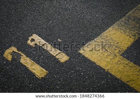 sign on the asphalt, yellow painted number eleven on grey street, yellow lines like a corner on the road, space for text 
