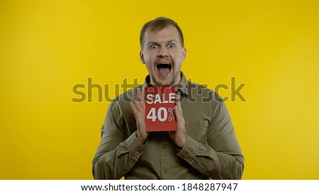 Attractive joyful blonde man showing Sale 40 percent Off inscriptions signs, rejoicing good discounts, low prices for online shopping sales. Studio shot on yellow background