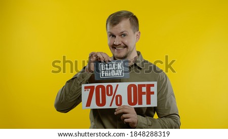 Shocked amazed emotions of store client. Man showing Black Friday and Up To 70 Percent Off inscriptions signs. Good holiday discounts, low prices for shopping. Yellow background