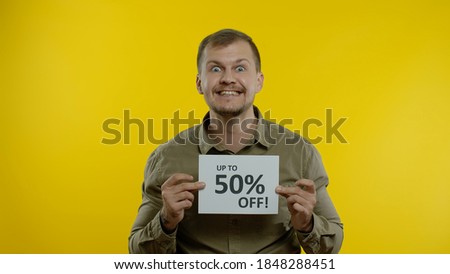 Excited smiling blonde man showing Up To 50 percent Off inscriptions signs, rejoicing good discounts, low prices for online shopping sales. Studio shot on yellow background
