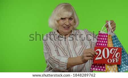 Grandmother showing 20 percent Off inscription sign and shopping bags. Senior woman smiling, looking satisfied with low prices, shopping on Black Friday, Christmas, New Year. Chroma key