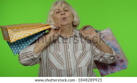 Happy senior grandmother raising shopping bags, celebrating, looking satisfied with purchase, enjoying discounts on Black Friday holiday. Elderly woman isolated on chroma key background
