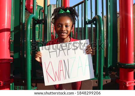 Beautiful black child holding Happy Kwanzaa Sign outdoors red black background