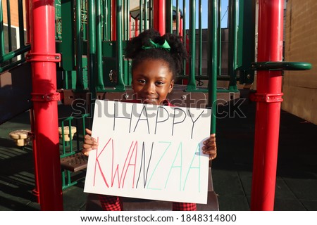 Smiling black girl holding happy Kwanzaa Sign outdoors in park