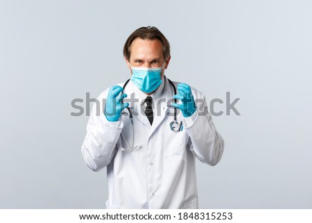 Covid-19, preventing virus, healthcare workers and vaccination concept. Mad annoyed doctor sick and tired of people not following social distancing rules, clench fists angry, wear mask and gloves