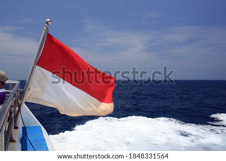 The red and white flag of Indonesia is flying at the stern of a ship traveling on the ocean