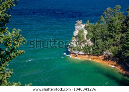 Upper Michigan lakeshore showing beautiful pictured rock beaches and bright green pines. The blue water sparkles on this summer day.