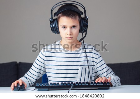 Portrait of child with headphones and keyboard sitting at home on computer, looking at the screen.