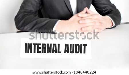 Businessman sitting at the table and signboard with text INTERNAL AUDIT