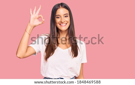 Young hispanic woman wearing casual white tshirt smiling positive doing ok sign with hand and fingers. successful expression. 