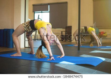 Beautiful young woman working out in loft interior. Doing yoga exercise on blue mat. Stretching. Standing in Bridge Pose.
