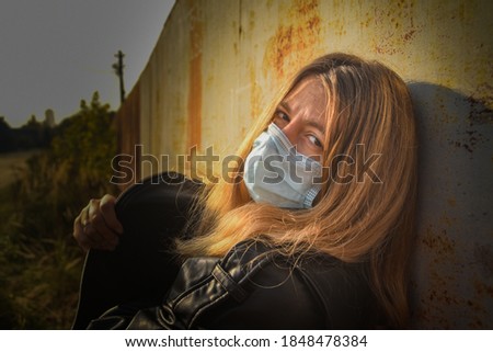 Woman wears medical mask near a rusty iron wall. Woman in medical mask looking at the camera