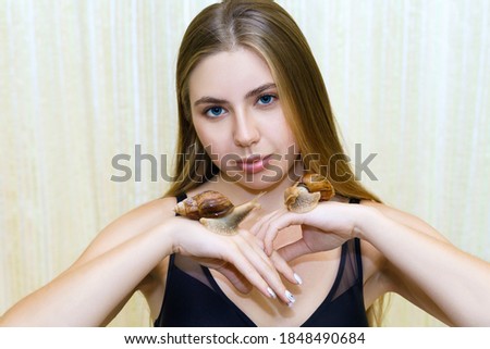 Young woman with clean healthy skin holds large snails in her palms after cleansing and rejuvenating facial skin. A new unconventional method for facial skin rejuvenation.