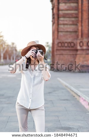 Female freelance professional photographer. Tourist woman traveling with a vintage camera taking a picture outdoors. Solo traveler photographing Barcelona city in Spain. Summer Vacation in Europe.