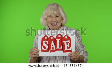 Joyful grandmother lady showing Sale word inscription note, smiling, looking satisfied with low prices, shopping on Black Friday. Senior woman rejoicing good discounts. Chroma key