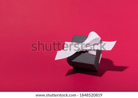 Black Friday sale concept. Black color gift box with white ribbon on red pink background. Valentine's Day, Christmas, Birthday, Mother's Day. Copy space.