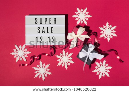 12.12 Super Sale text on white Lightbox, black and red gift boxes, white snowflakes on red paper background. Double 12 Mega sales day concept. Online shopping of China. Top view, copy space.