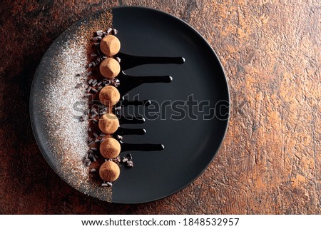 Chocolate truffles on a black plate with chocolate sauce. Sweets are sprinkled with cocoa powder and powdered sugar. Top view. 