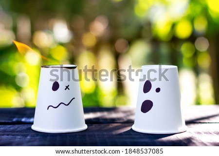 Two white cups with painted emotions. Burning glass. A symbol of relationships in society. Panic, problems, anxiety