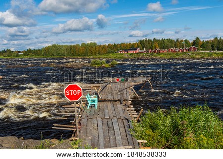 Bridge out to the rapid used for fishing with handle landing net,  with a stop sign as a warning, blue sky and clouds in background, picture from kukkola rapid in Torne river Norrbotten Sweden.