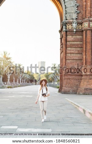Female solo traveler holding a vintage camera while walking around the city of Barcelona in a nice outfit with a hat. Amateur photographer enjoying taking pictures	