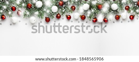 Christmas snow border of shiny white and red balls, evergreen branches on a white wooden background. New year card, banner.