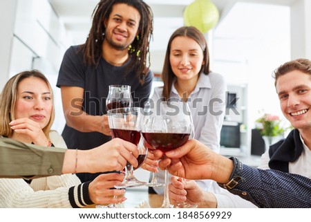 Happy group of friends toasts together with a glass of red wine in the kitchen, celebrating