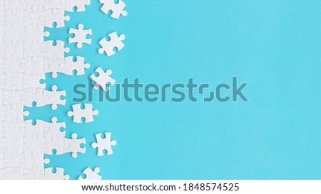 Assembling jigsaw puzzle pieces, Top view unfinished white jigsaw puzzle on blue background, Fragment of a folded white jigsaw puzzle with copy space, Teamwork and problem solving concept.  Royalty-Free Stock Photo #1848574525