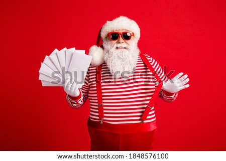 Photo of grandfather grey beard smile have fun hand hold envelopes wear santa claus x-mas costume suspenders sunglass striped shirt cap gloves isolated red color background