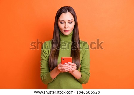Photo of young beautiful serious calm charming pretty lovely girl use phone chatting isolated on orange color background
