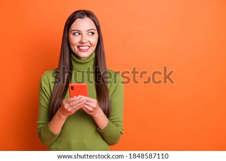 Photo of young beautiful smiling cheerful positive lovely girl look copyspace hold smartphone isolated on orange color background