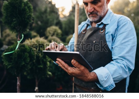 middle aged gardener working with digital tablet in tree nursery