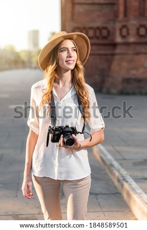 Portrait of a Tourist woman holding a vintage old camera outdoors. Female solo traveler wearing hipster outfit and fedora hat. Tourism agency campaign in Barcelona. Summer holidays in Europe
