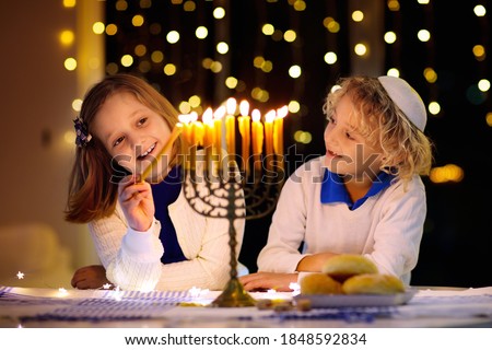 Kids celebrating Hanukkah. Jewish festival of lights. Children lighting candles on traditional menorah. Boy in kippah with dreidel and Sufganiyah doughnut. Israel holiday. Royalty-Free Stock Photo #1848592834