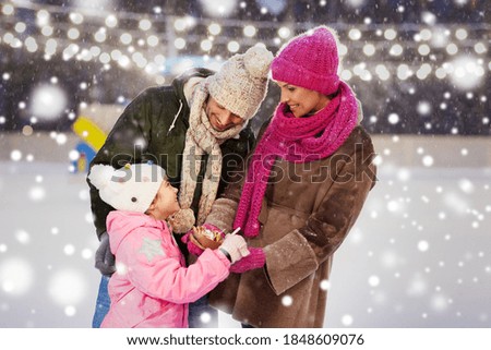 christmas, family and leisure concept - happy mother, father and daughter eating takeaway pancakes at outdoor skating rink in winter over snow