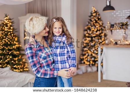 Mother and her daughter hugs in checked shirts. Morning Christmas. New Year's decor in living room. Xmas mood.  Weekend leisure togetherness. Motherhood childhood. white sweater. Family 