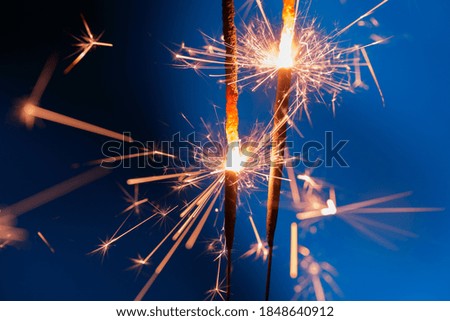 A pair of sparklers glow a soft yellow light against the overcast evening sky
