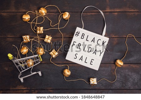 Black friday sale word on lightbox and small shopping cart with golden gifts on wooden background.