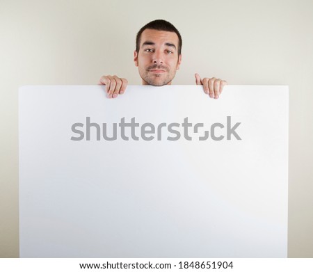 Studio photo of smiling man in his 30s holding a large blank paper sign. Isolated on bright background.
