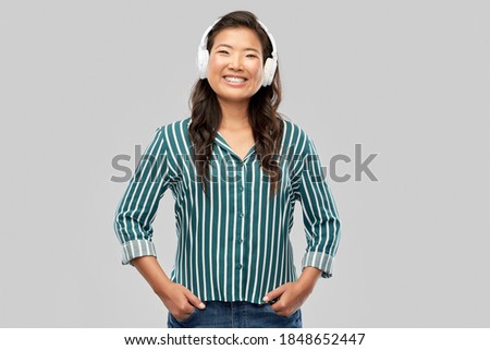 people, technology and audio equipment concept - happy young asian woman in headphones listening to music over grey background