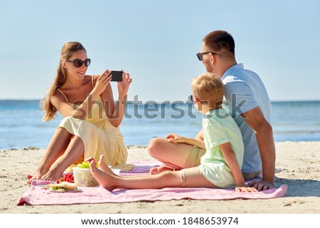 family, leisure and people concept - happy mother with smartphone photographing father and son on summer beach