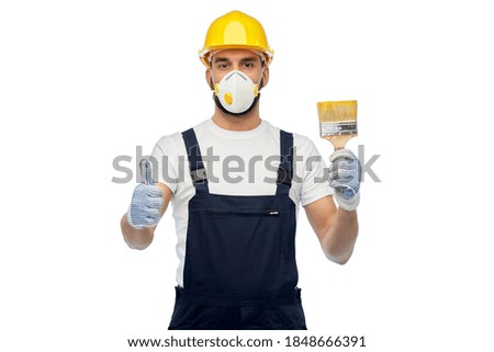 profession, construction and building - male worker or builder in yellow helmet and respirator with brush showing thumbs up over white background