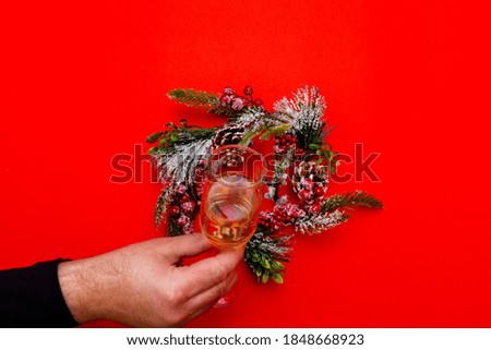 Top view one male hand holds glass of champagne, flat lay wreath on a red background