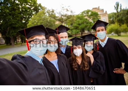 Photo portrait of six graduates taking selfie wearing face masks outside university