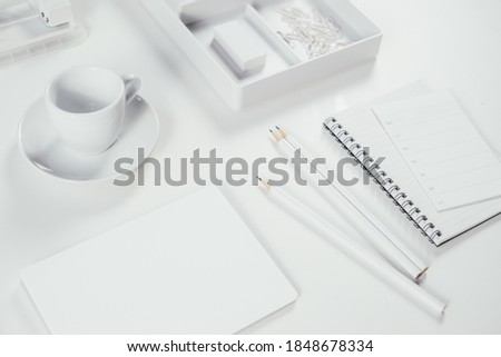 Pencils on a white desk next to a notepad, an espresso cup and office supplies, layout out in an organized, all-white, minimalist fashion. 