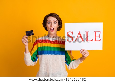 Photo of surprised girl hold sale poster show credit card open mouth wear striped sweater isolated yellow color background